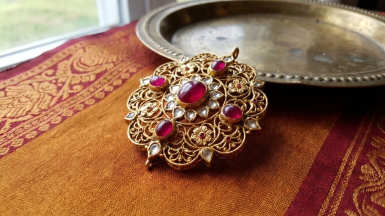Intricate Indian gold pendant set with cabochon rubies resting on traditional patterned silk fabric