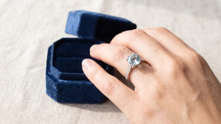 Cushion-cut aquamarine engagement ring worn on a hand beside an open blue velvet box