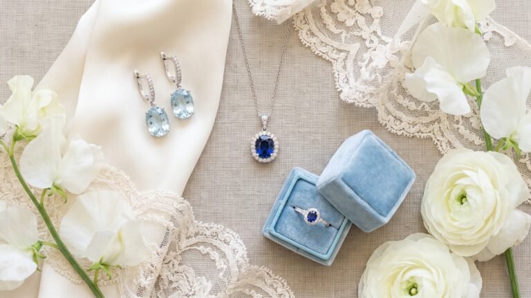 Blue sapphire necklace and ring in velvet box with aquamarine earrings, white flowers, and lace textiles