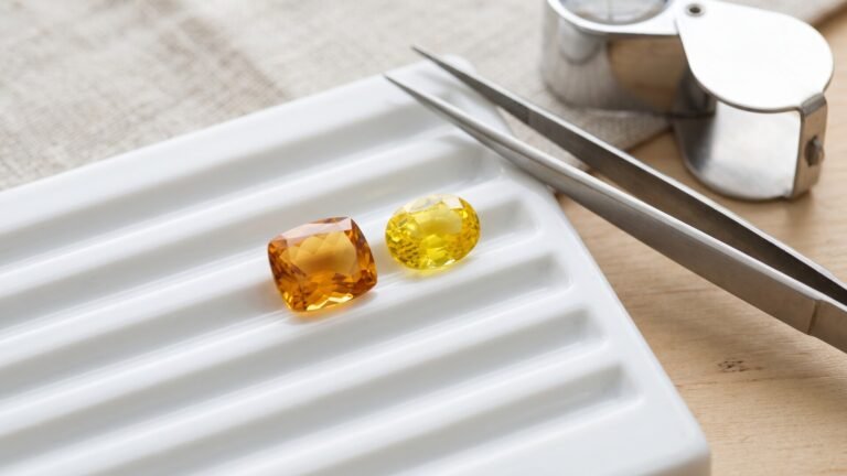 Faceted cushion citrine and oval yellow sapphire resting on a white gem sorting tray next to tweezers