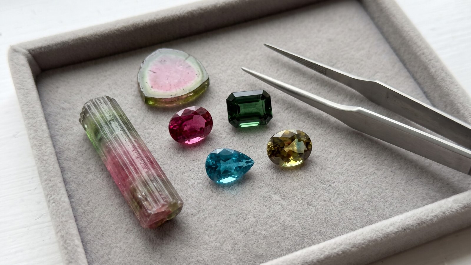 Collection of rough, sliced, and faceted tourmaline gemstones in various colors on a sorting tray with tweezers