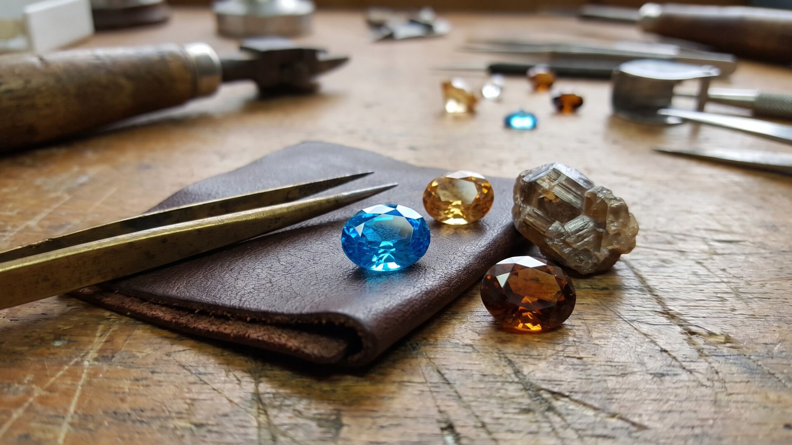 Faceted blue, yellow, and brown zircon gems beside a rough crystal on a jeweler's workbench