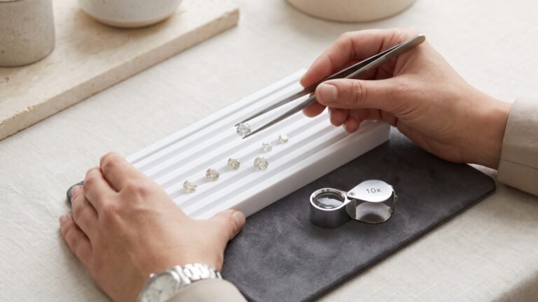 Gemologist using tweezers to inspect loose cut diamonds on a grading tray beside a 10x loupe