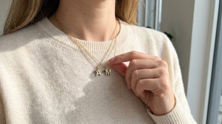 Woman wearing layered gold chain necklaces with A and M initial charms set with blue and green birthstones
