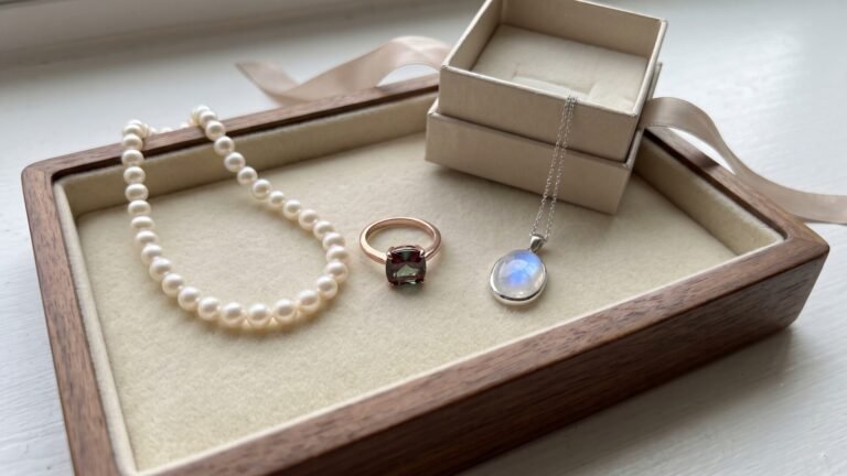 Pearl necklace, alexandrite ring, and moonstone pendant arranged on a wooden jewelry tray