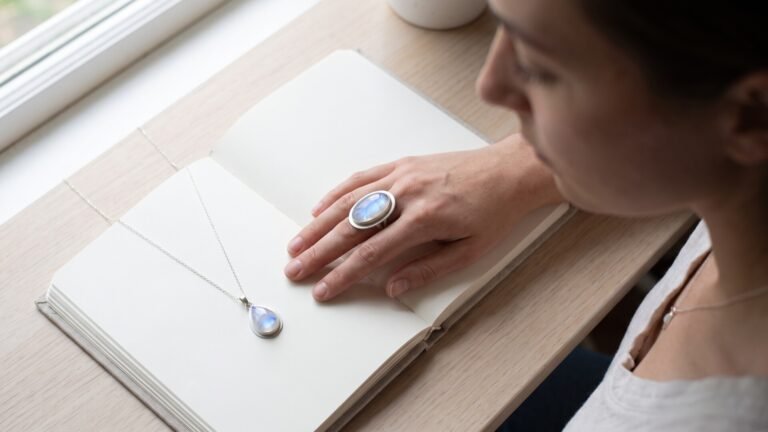 Woman wearing an oval moonstone ring beside a teardrop moonstone necklace resting on an open journal