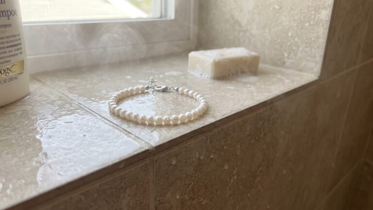 White pearl birthstone bracelet resting on a wet tiled shower ledge beside a bar of soap