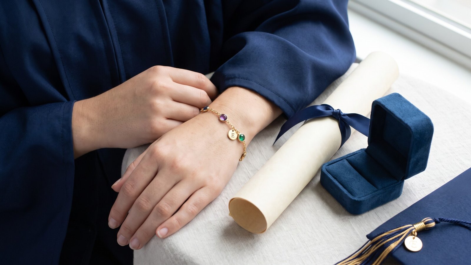 Graduate wearing a gold personalized birthstone bracelet next to a diploma and jewelry box