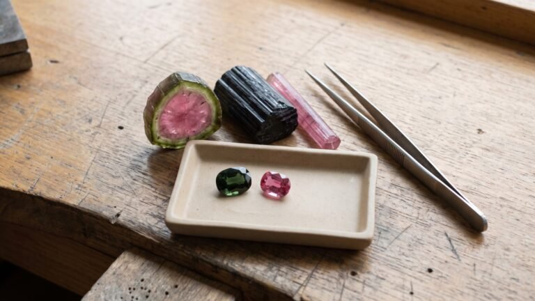 Raw watermelon tourmaline, black crystal, and faceted green and pink gems on a jeweler workbench
