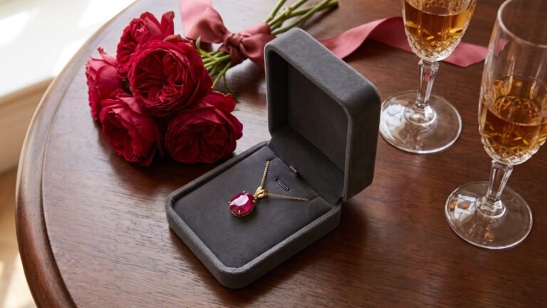 Ruby pendant necklace in a velvet box beside red roses and champagne glasses for a 40th anniversary celebration
