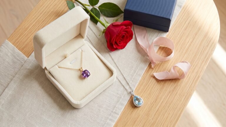 Amethyst and aquamarine birthstone pendant necklaces displayed with a red rose and gift boxes on a table