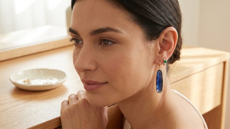 Woman wearing a dangling blue gemstone drop earring paired with a small green birthstone stud